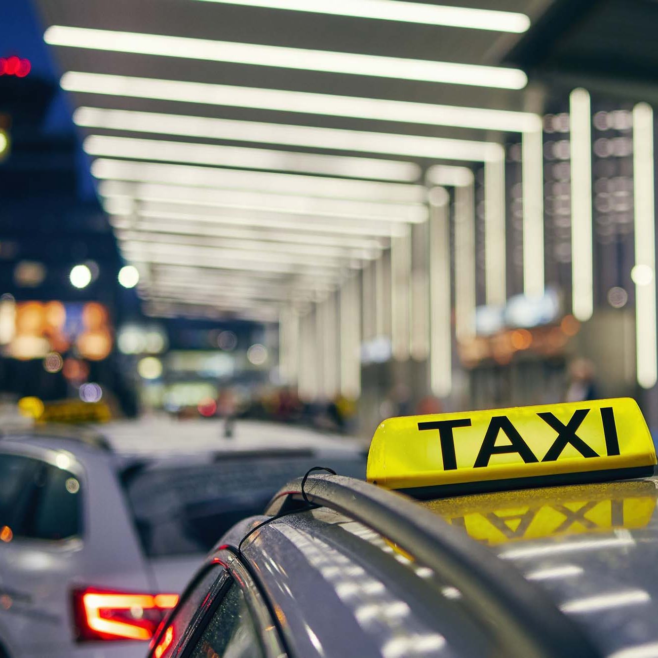 Lighting taxi sign on the roof of car against airport terminal at night.